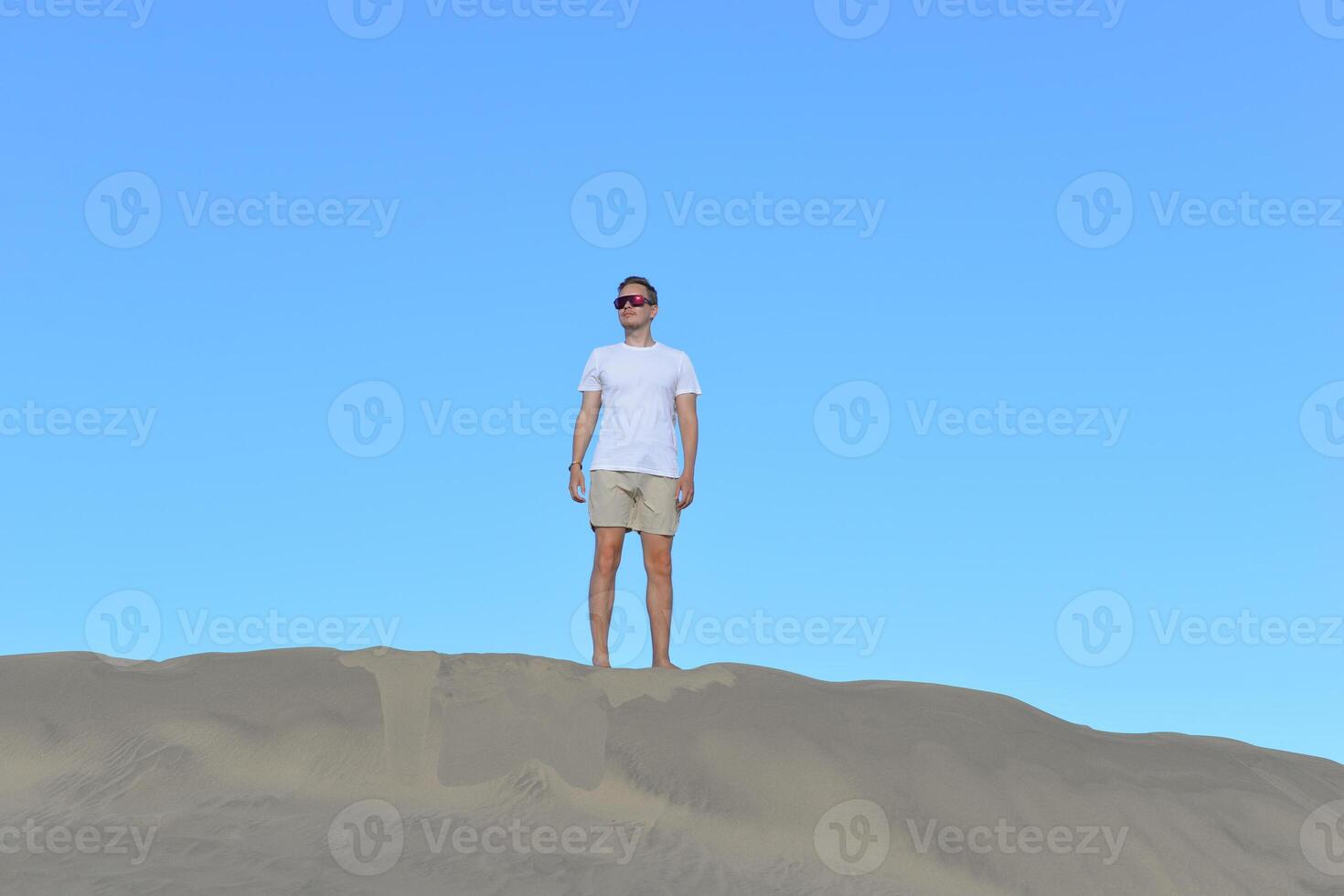 A young man walking along a sand dune through barkhan in Maspalomas, Gran Canaria. A self confident man goes up the mountain - success and achievements concept photo