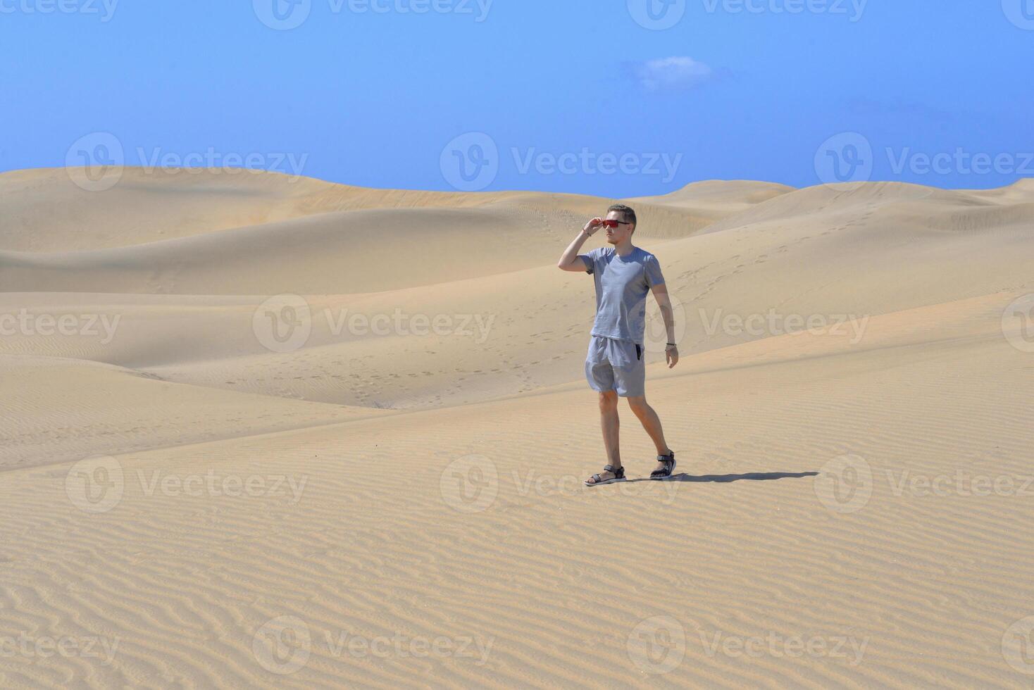 A man walking along a sand dune through barkhan in Maspalomas, Gran Canaria on a hot sunny day. Desert travel touristic concept photo