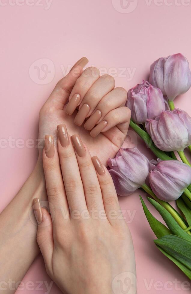 Woman showing nude manicure and purple tulips on pink background photo