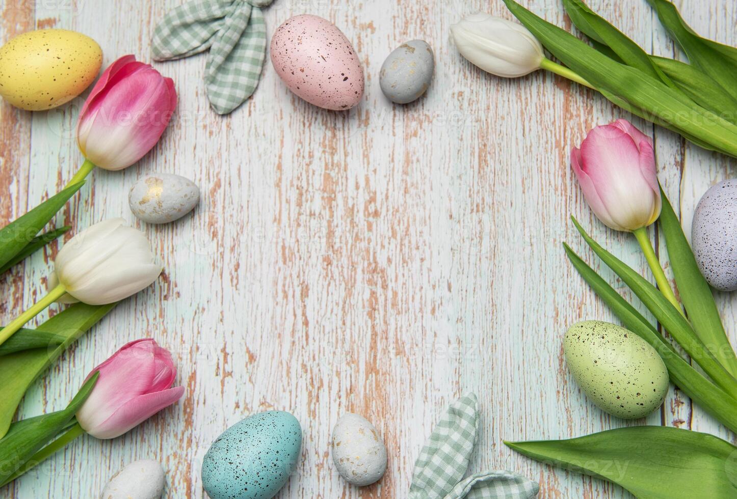 Easter eggs and tulips creating a frame on wooden background photo