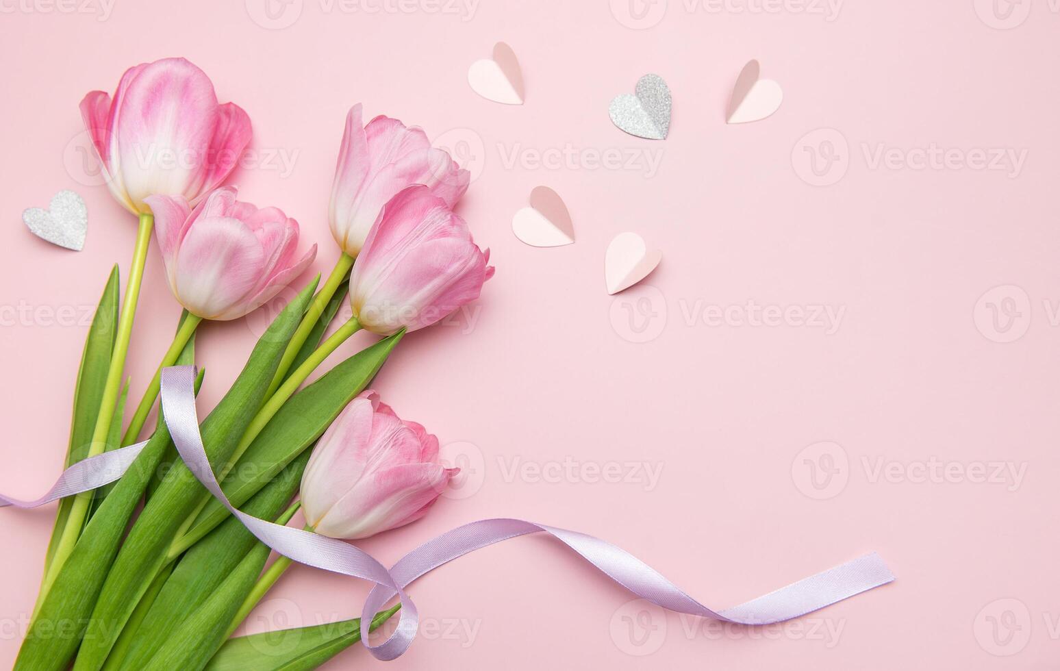 Pink tulips with purple ribbon and paper hearts creating lovely composition on pink background photo