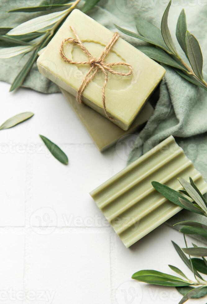 Natural olive soap bars with olive branches on white tiles photo