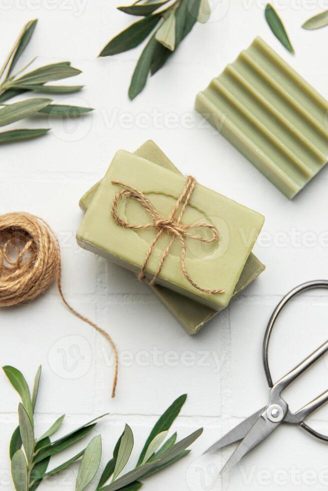 Natural olive soap bars with twine and scissors on white tile background photo