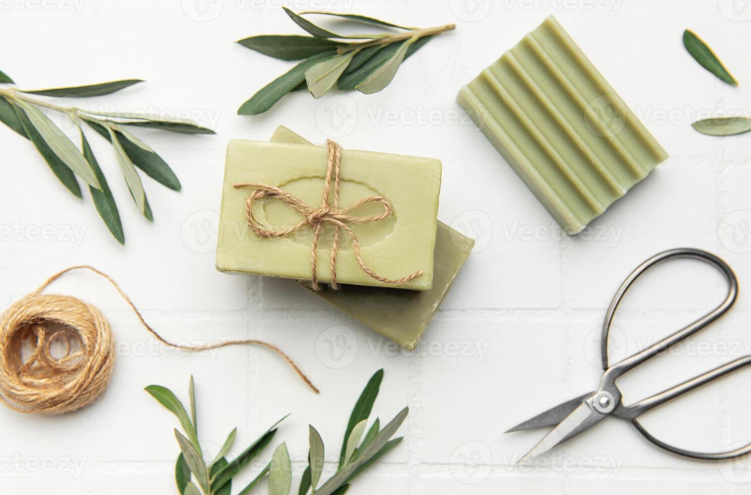 Olive soap bars with twine and scissors on white tile background photo