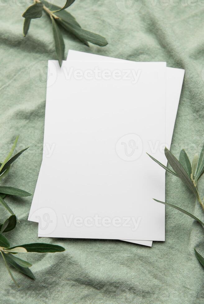 Cards resting on green fabric with olive branches for elegant invitation or announcement photo