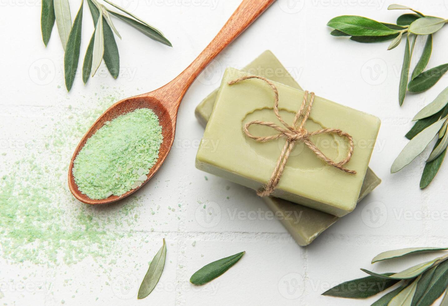 olive soap bars with green bath salt and olive leaves on white tile background photo