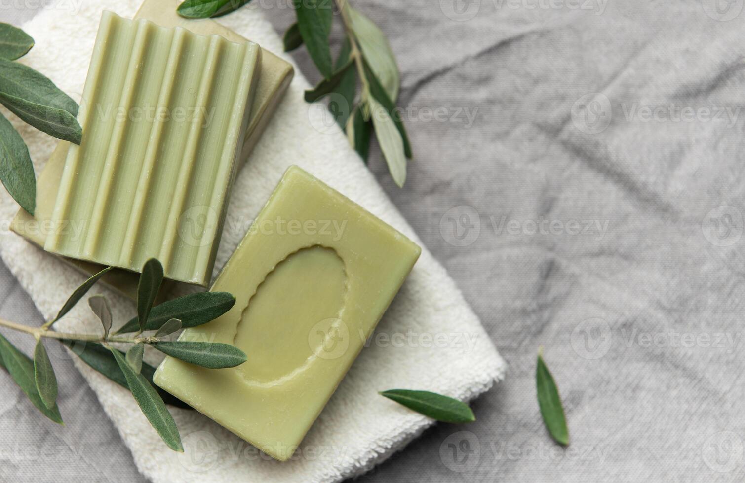 Olive soap bars resting on soft white towel with fresh olive branches photo