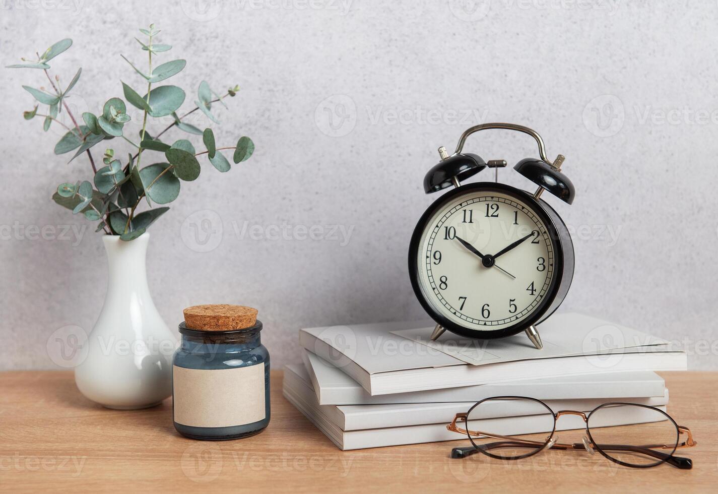 Alarm clock, books, eyeglasses, candle and eucalyptus branches on wooden desk photo