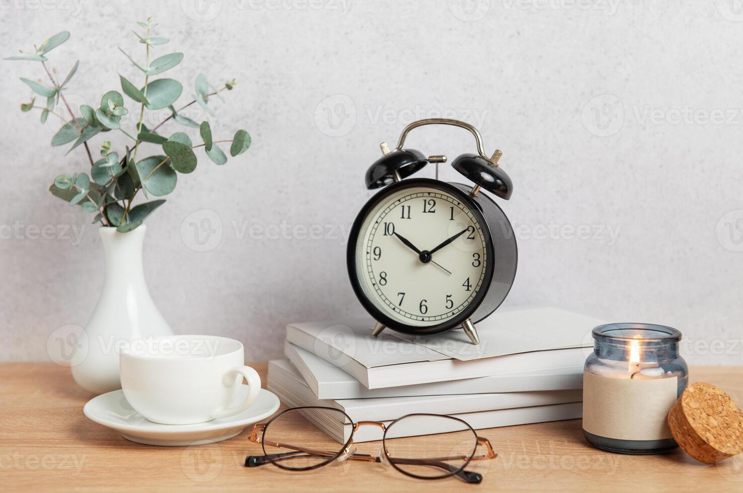 Alarm clock, books, coffee cup, eyeglasses and candle creating cozy atmosphere on wooden desk photo