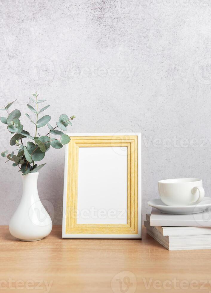 Empty photo frame, eucalyptus leaves, books and coffee cup on table
