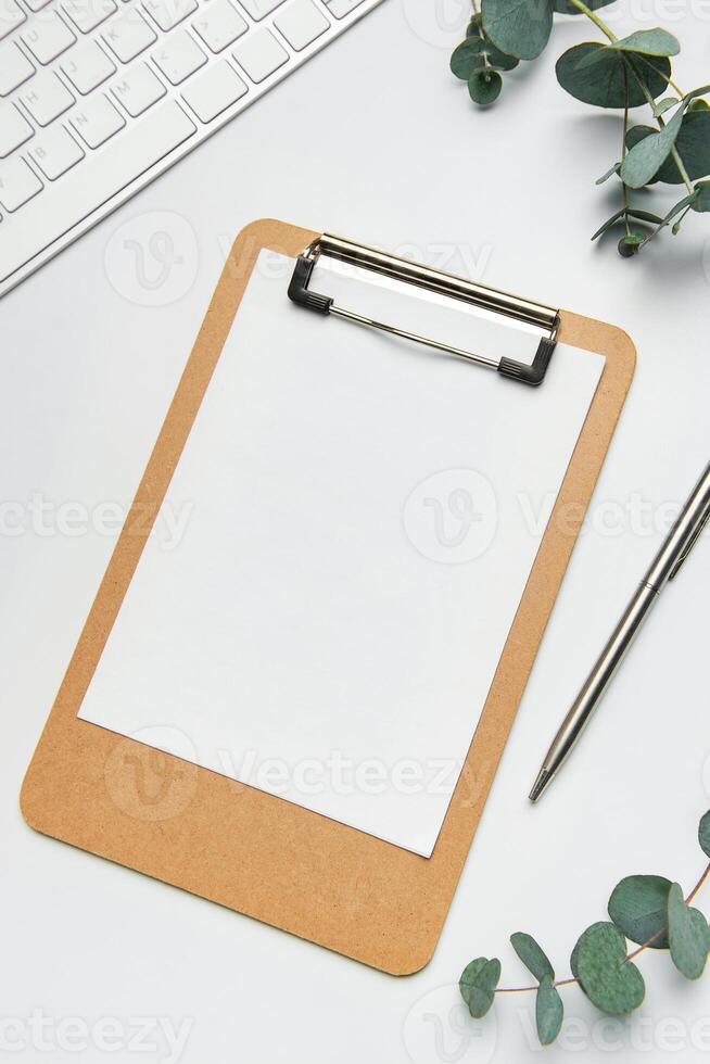 Clipboard with paper, pen, keyboard and eucalyptus branches on white table for working or studying photo