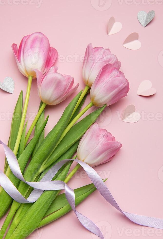 Pink tulips with ribbon and paper hearts creating lovely composition on pink background photo