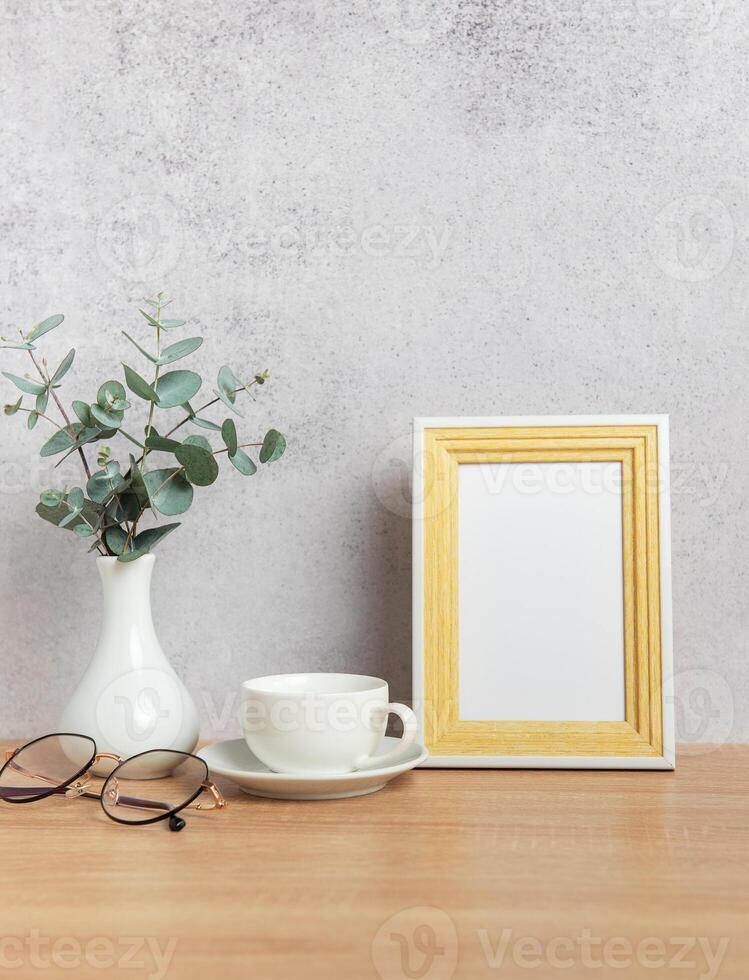 Eucalyptus branches, coffee cup, eyeglasses and empty frame creating cozy atmosphere on table photo