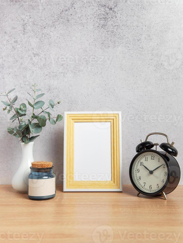 Photo frame, alarm clock, eucalyptus branches and jar on wooden table