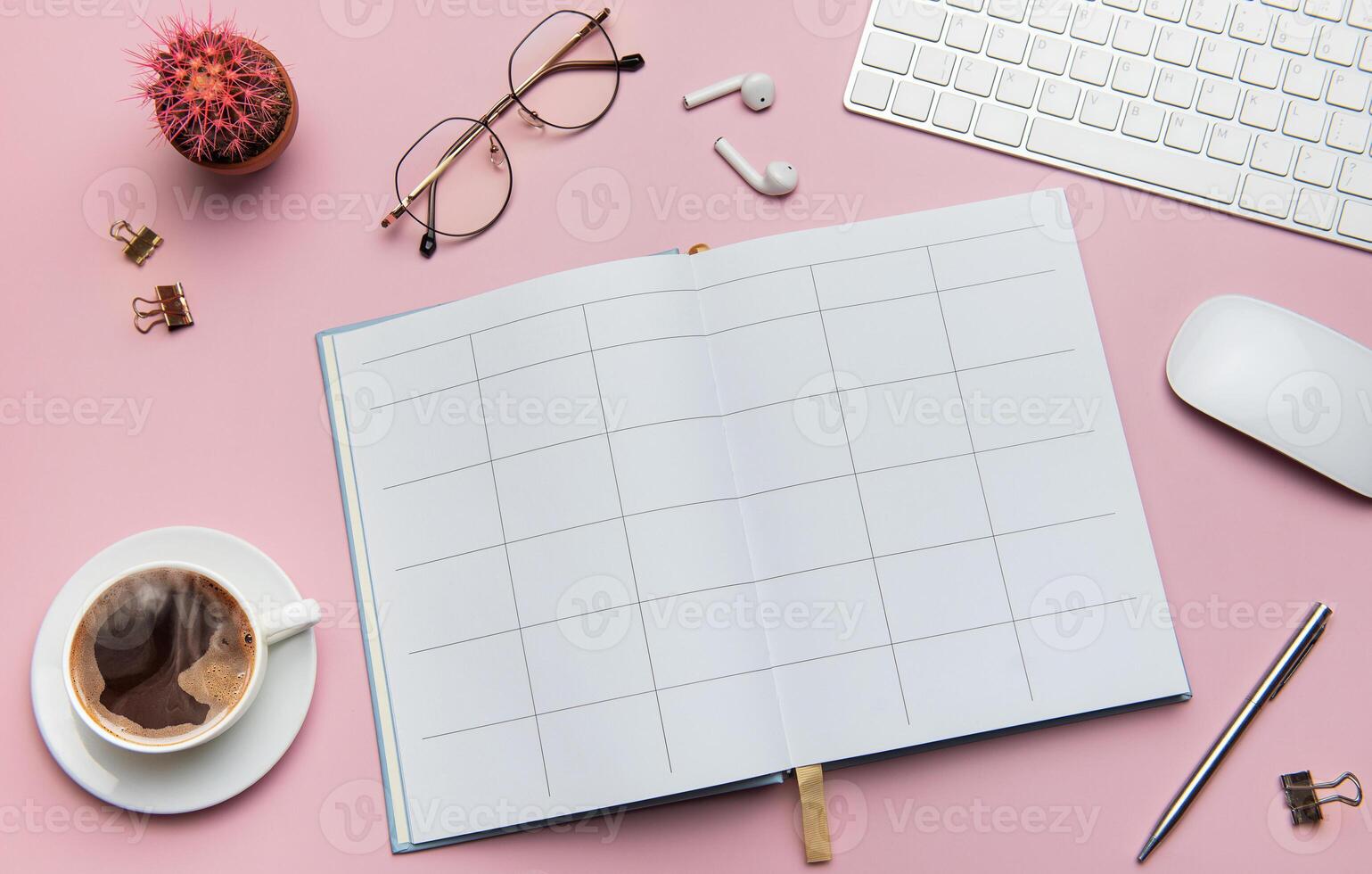 Open notebook, coffee, cactus, glasses, earphones, pen, keyboard and mouse lying on pink table photo