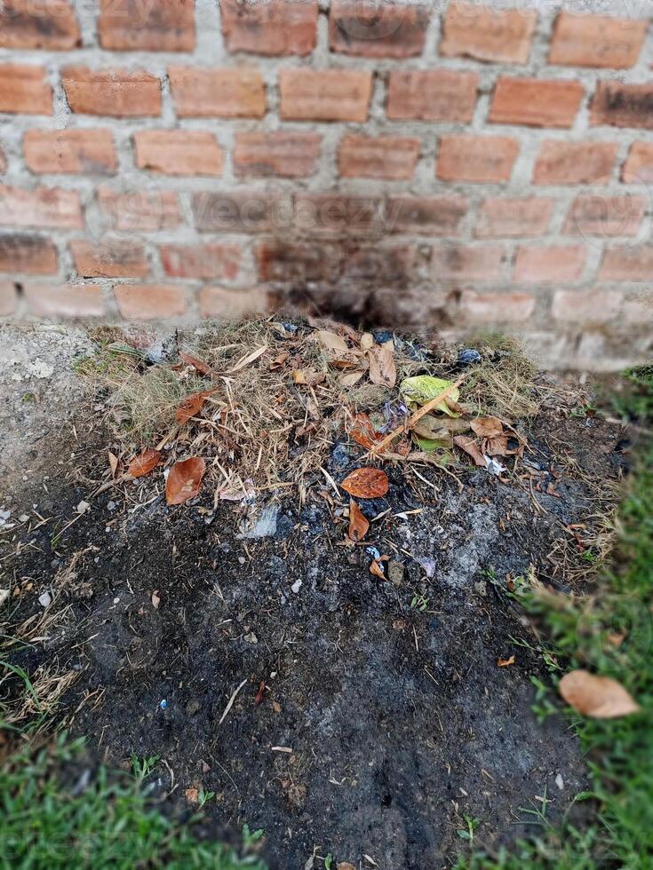A pile of burned trash sits at the base of a brick wall photo