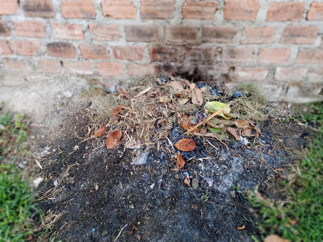 A pile of burned trash sits at the base of a brick wall. photo