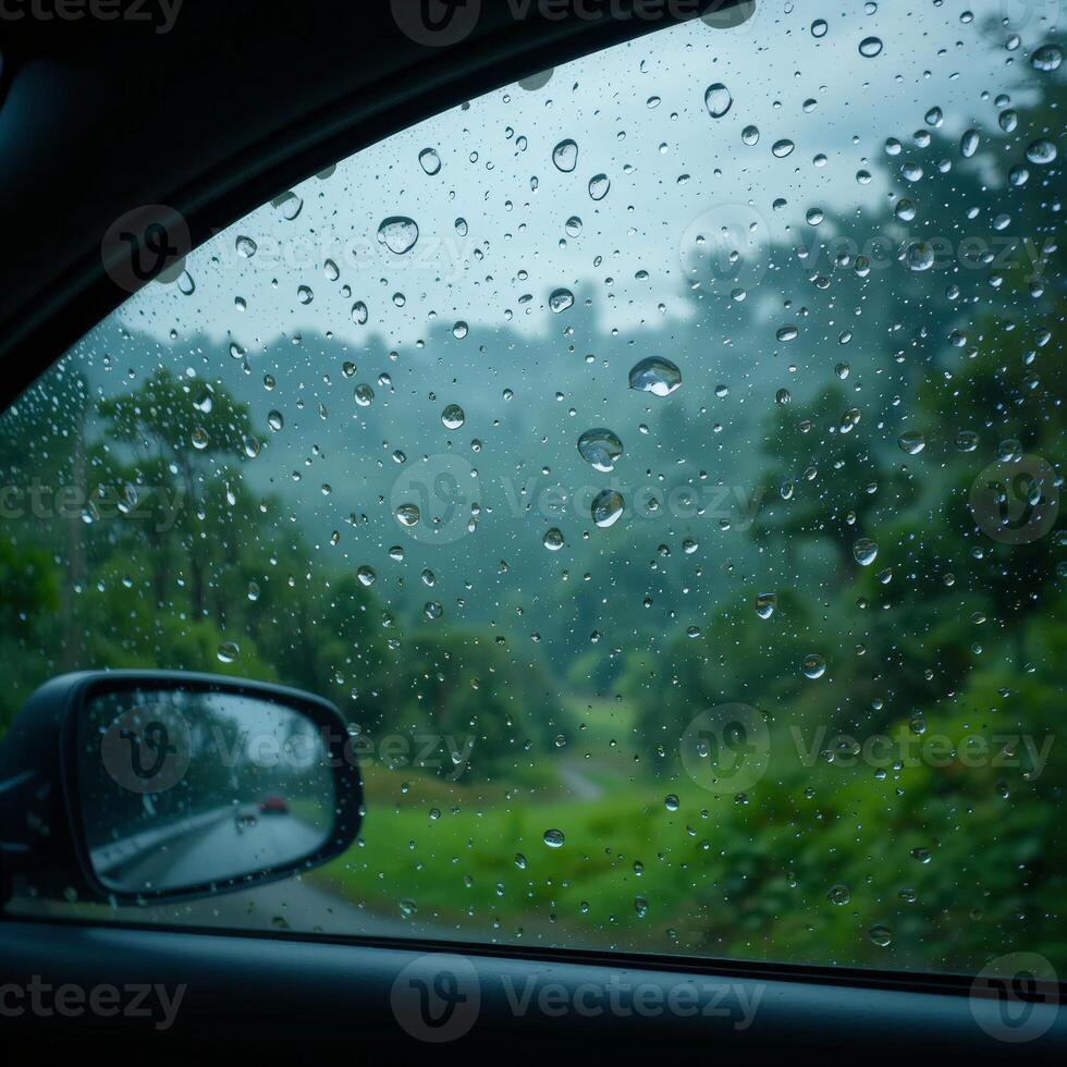Raindrops scatter over a car window, blurring a lush green landscape seen through the glass. The scene captures a peaceful moment of nature during a rainy drive. photo