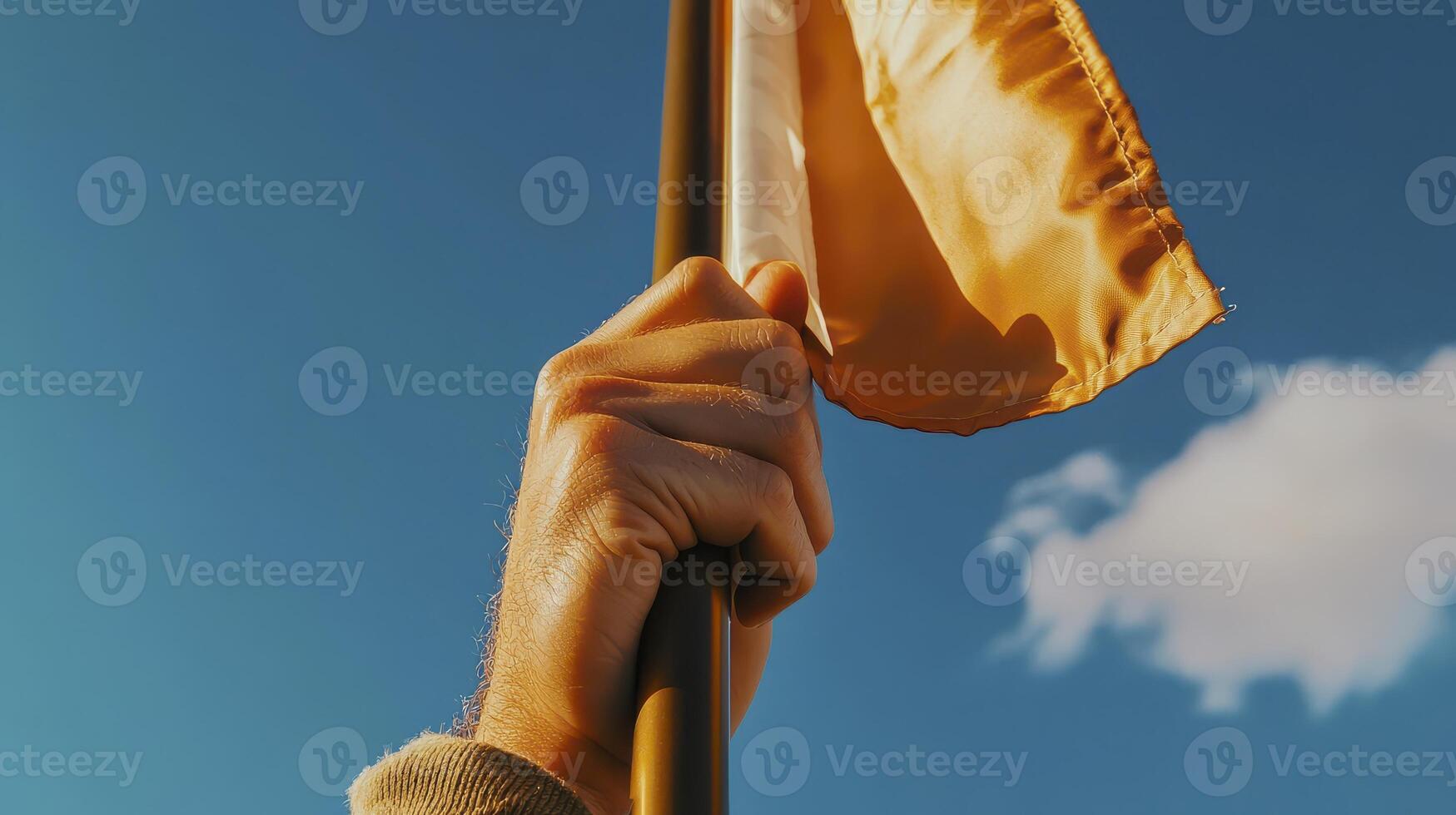 Close Up Hand Holding Golden Flag Against Blue Sky photo