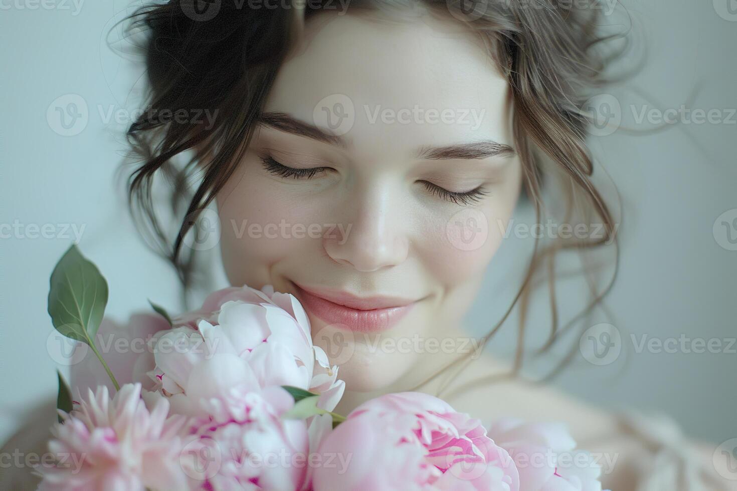 close up of young tender smiling woman enjoying smell of bouquet of pink peonies flowers on light neutral background photo