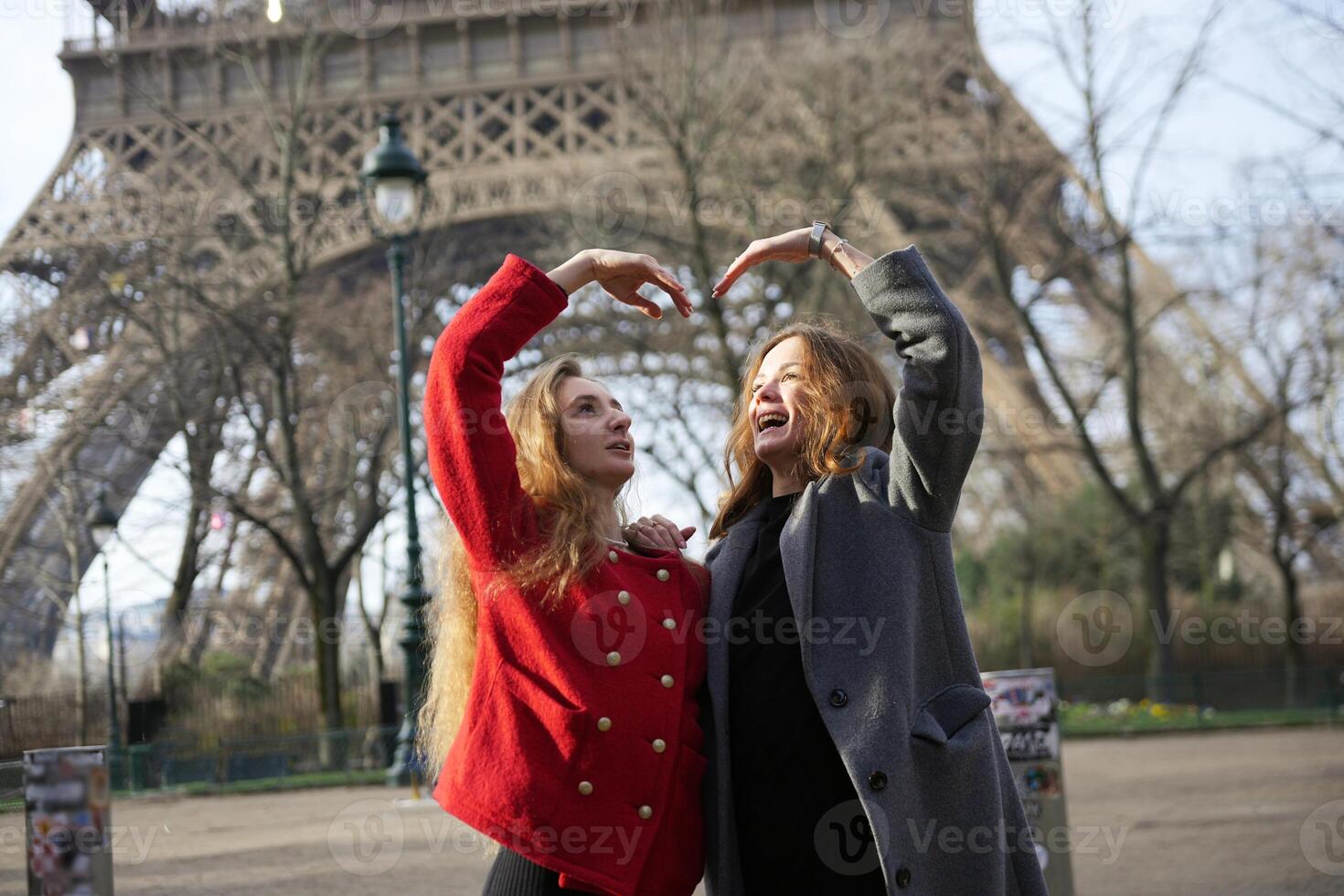 Two female friends form a heart shape with their hands in front of the Eiffel Tower, symbolizing love and friendship in Paris. photo