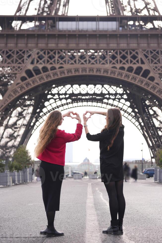 Two women making heart shape under Eiffel Tower photo