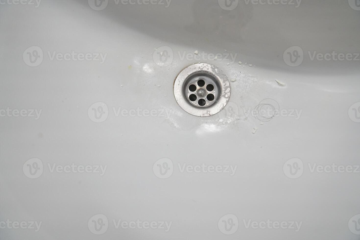 View of a metal drain in a white ceramic bathroom sink. With space to copy photo