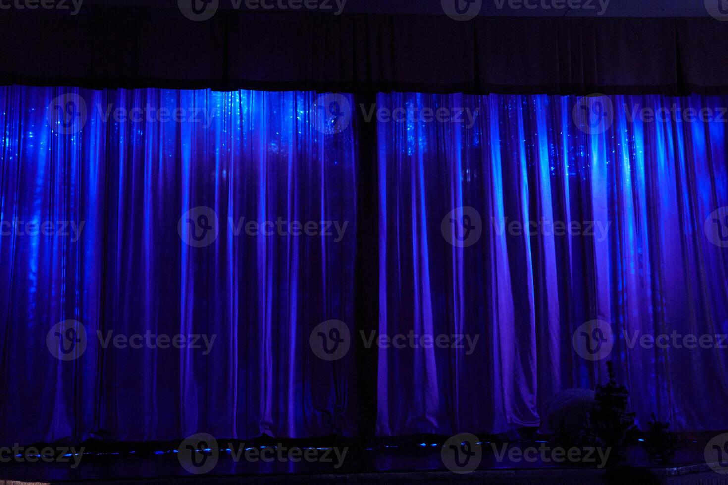A stage with closed curtains, waiting for the artists to perform. Blue lamps are shining on the stage. With space to copy photo