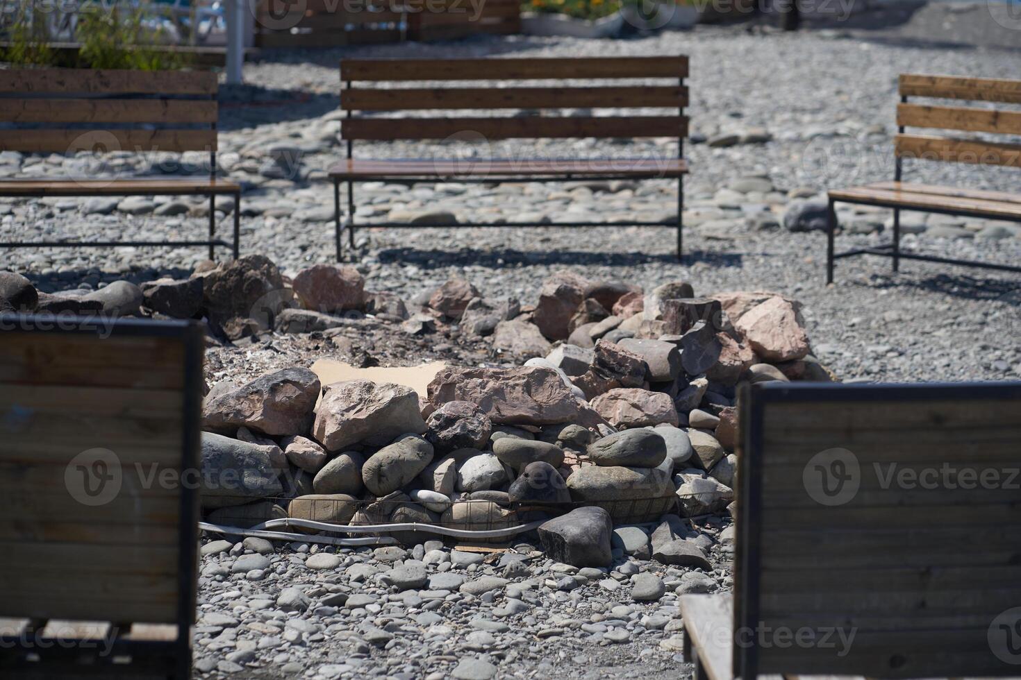 The serene setting with an extinguished bonfire surrounded by wooden benches creates a peaceful atmosphere against a stone background. photo