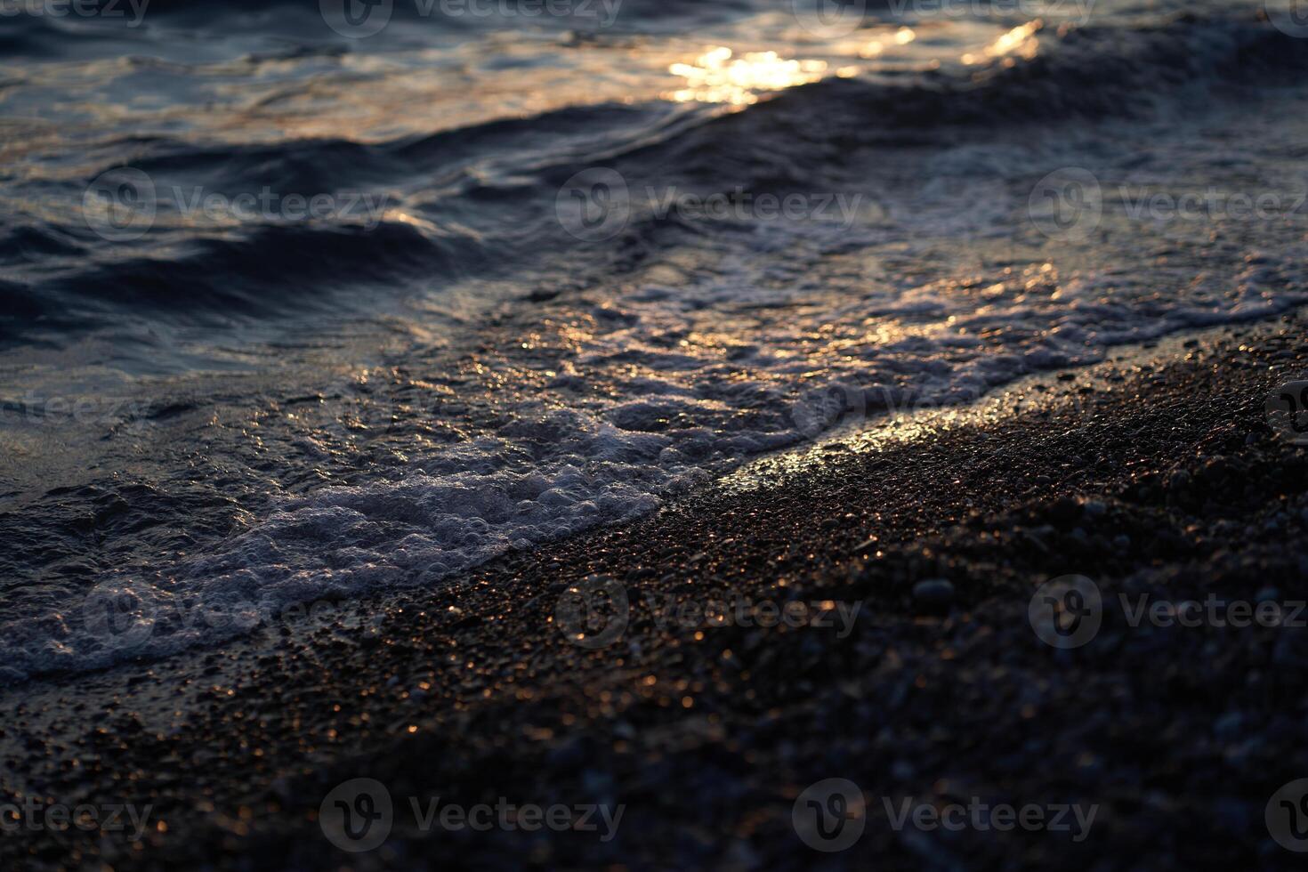 The sea at dusk. Water reaching the shore of a pebble beach in the afternoon sun. With space to copy photo