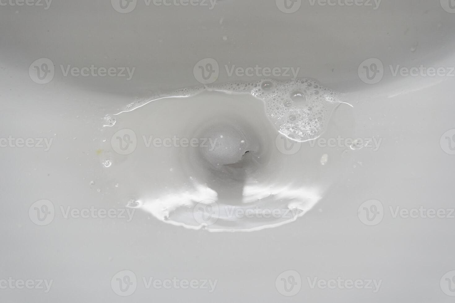White ceramic bathroom sink with water that goes down the drain. With space to copy photo