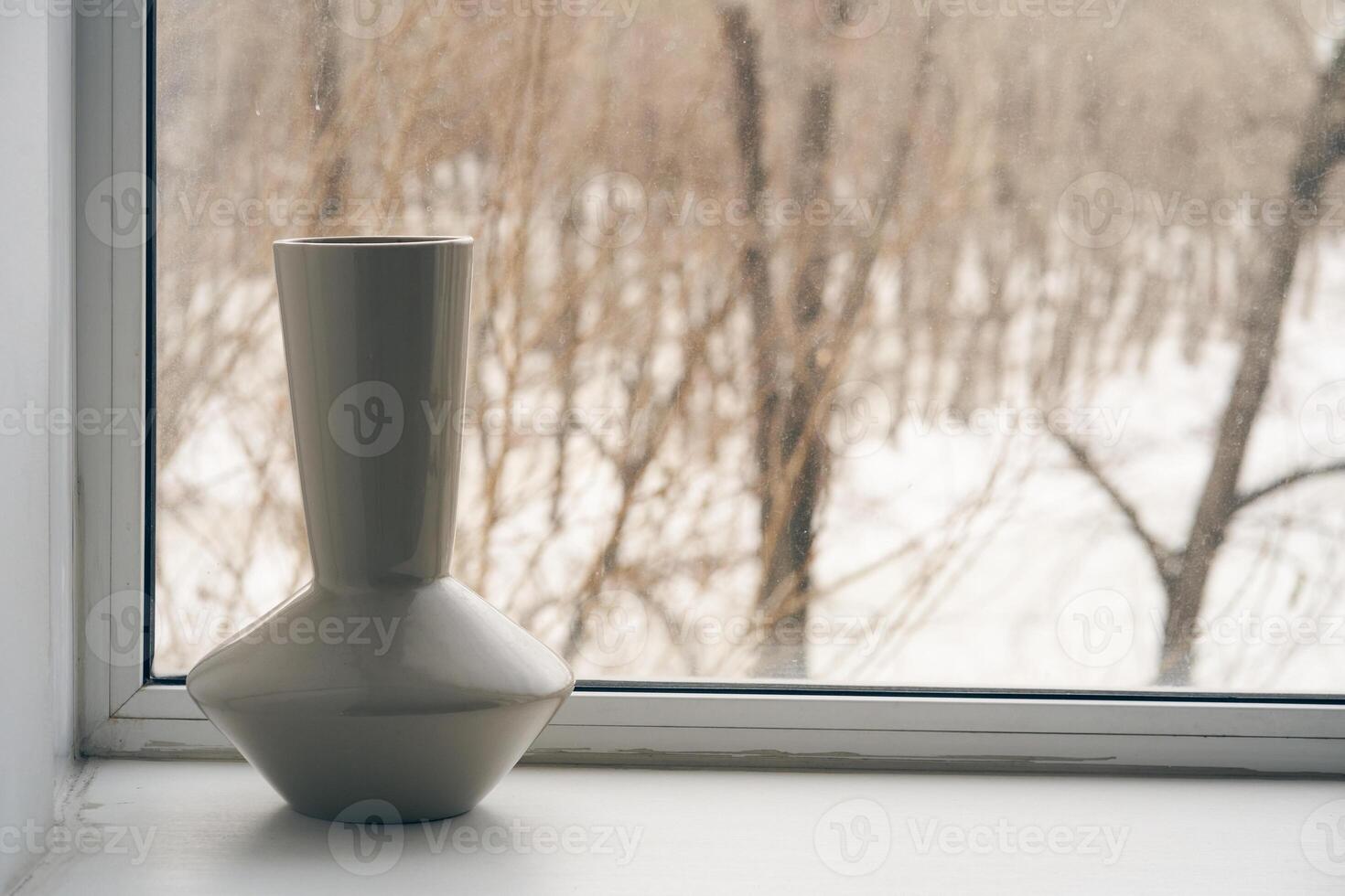 A single empty vase stands on the windowsill against the background of a frozen window in winter. The concept of frost and cold weather. photo