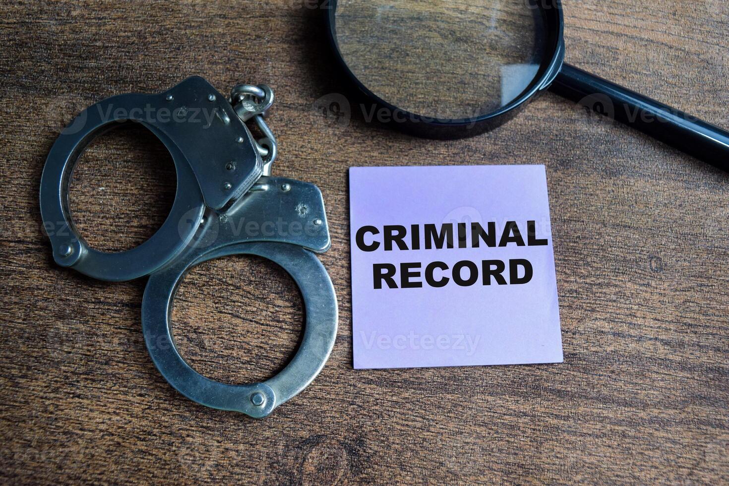 Concept of Criminal Record write on sticky notes and handcuff isolated on Wooden Table. photo