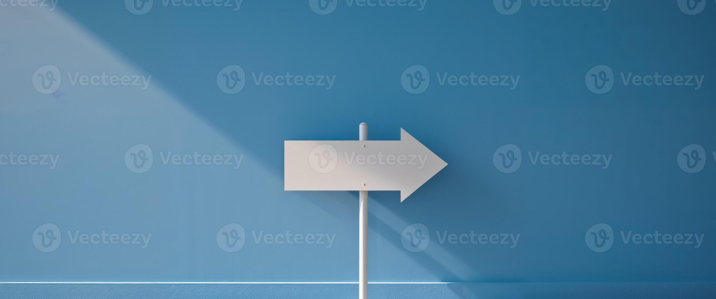 A white sign pointing to the right on a blue wall photo