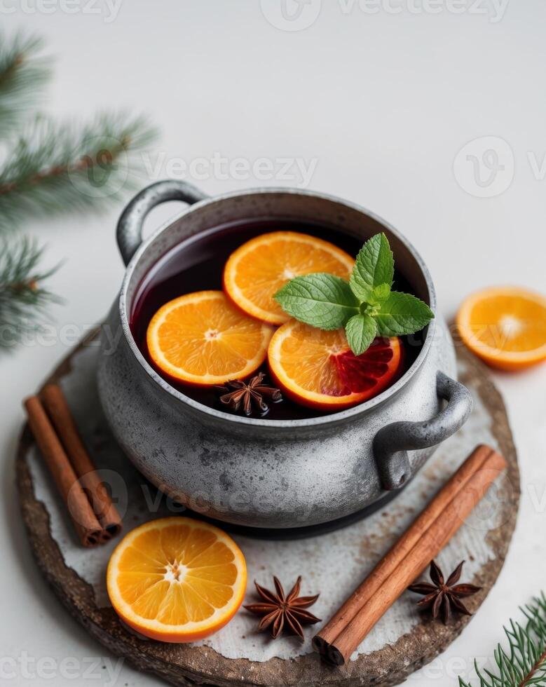 A Cozy Pot of Mulled Wine with Orange Slices and Mint Garnish Surrounded by Spices and Evergreen on a Rustic Wooden Coaster for Winter Warmth. photo