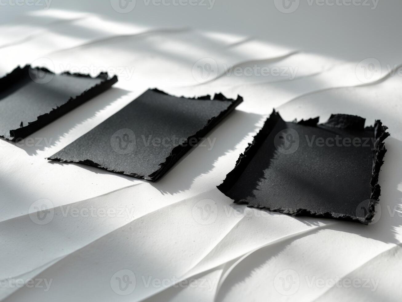 Three black papers with torn edges on a clean white surface photo