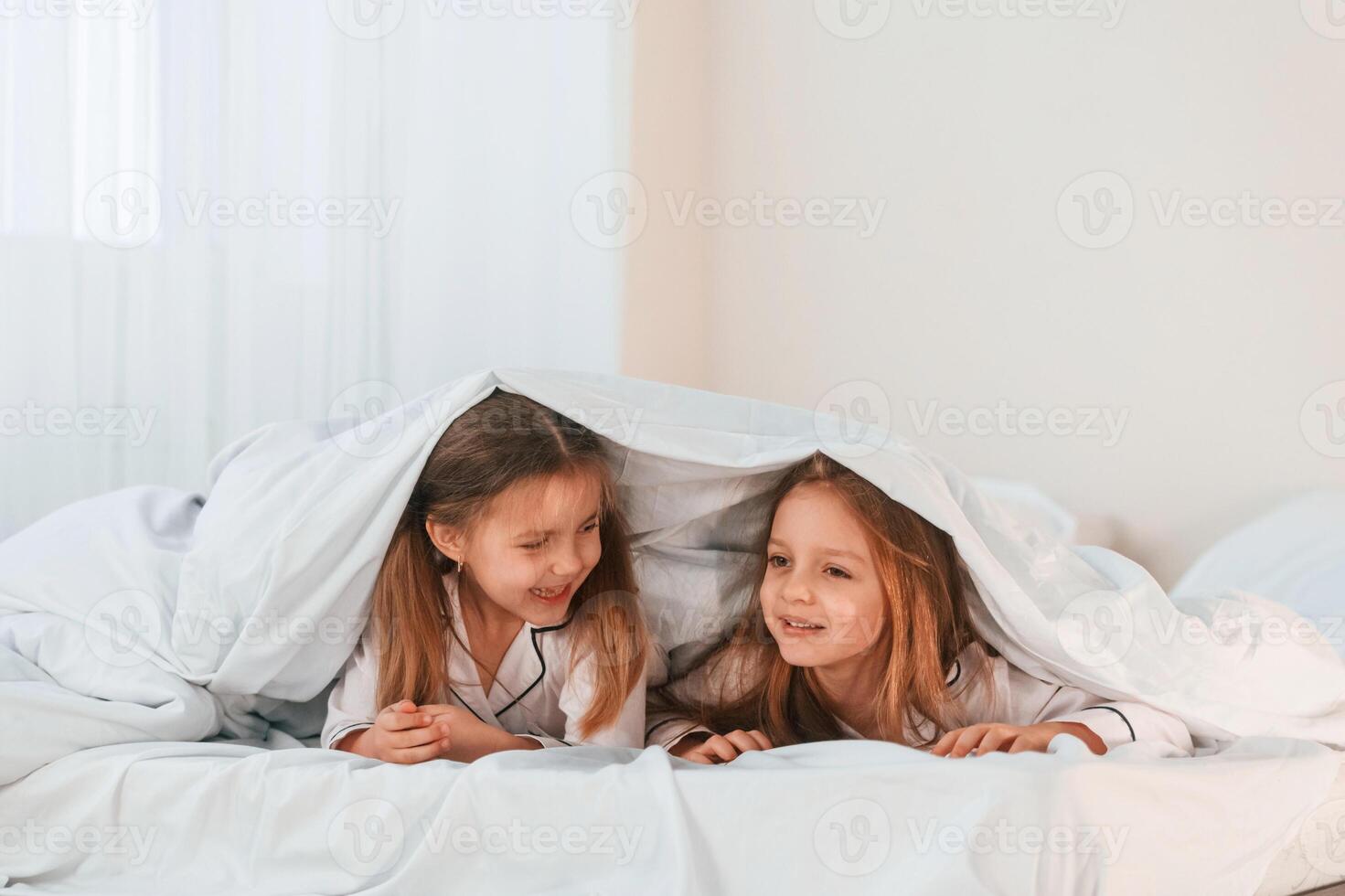 Lying down, on the bed. Two little girls are playing and having fun together in domestic room photo