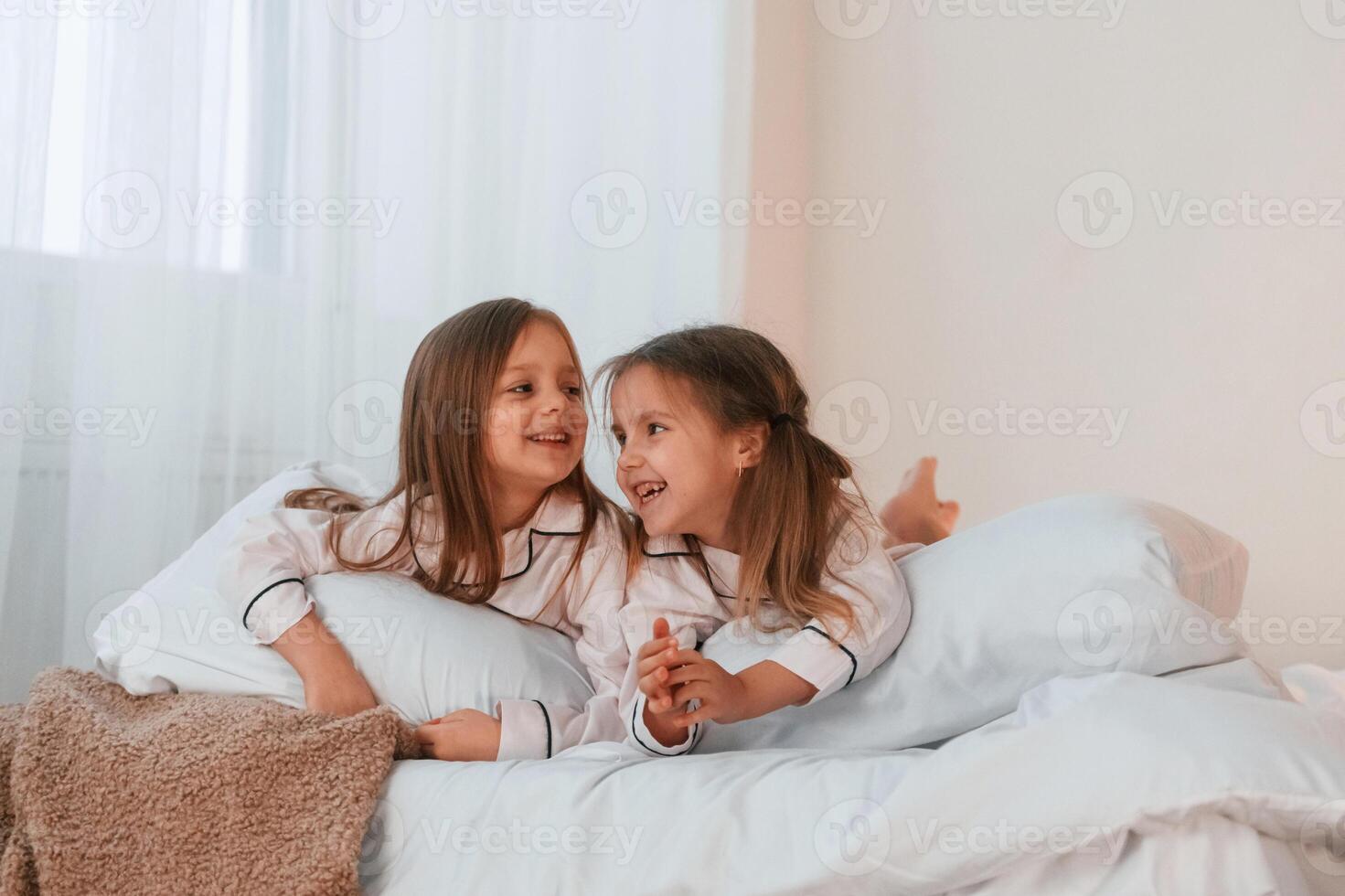 Lying down on, the bed. Two little girls are playing and having fun together in domestic room photo