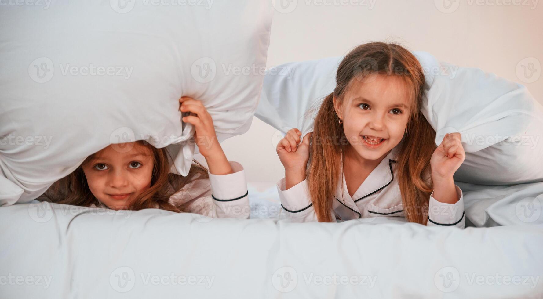 Kids are lying down ,on the bed. Two little girls are playing and having fun together in domestic room photo