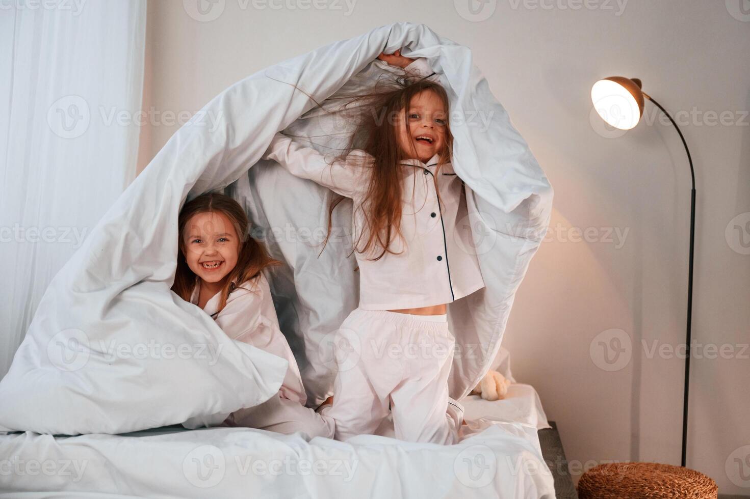 In the bedroom, with blanket in hands. Two little girls are playing and having fun together in domestic room photo