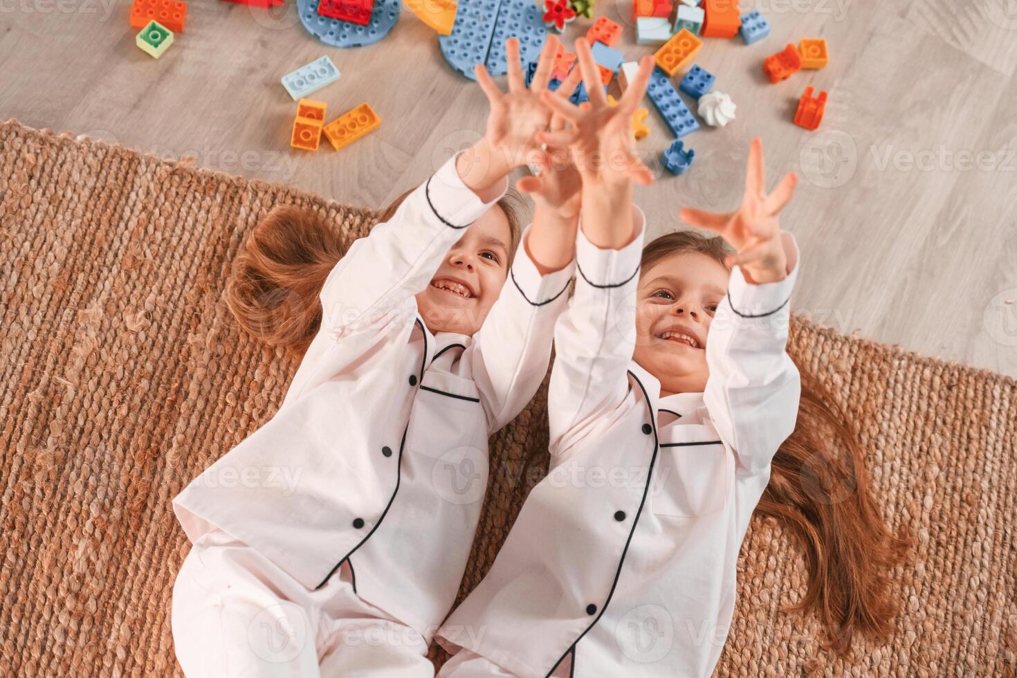 With hands up.. Lying down on the floor. Two little girls are playing and having fun together in domestic room photo