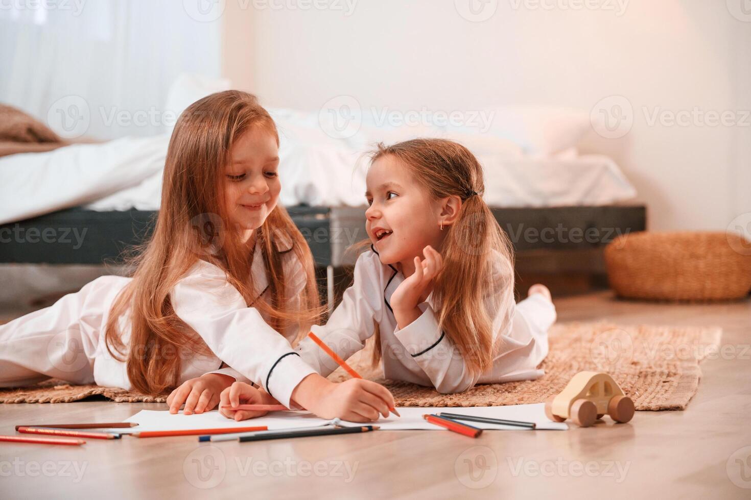 Drawing and lying down on the floor. Two little girls are playing and having fun together in domestic room photo