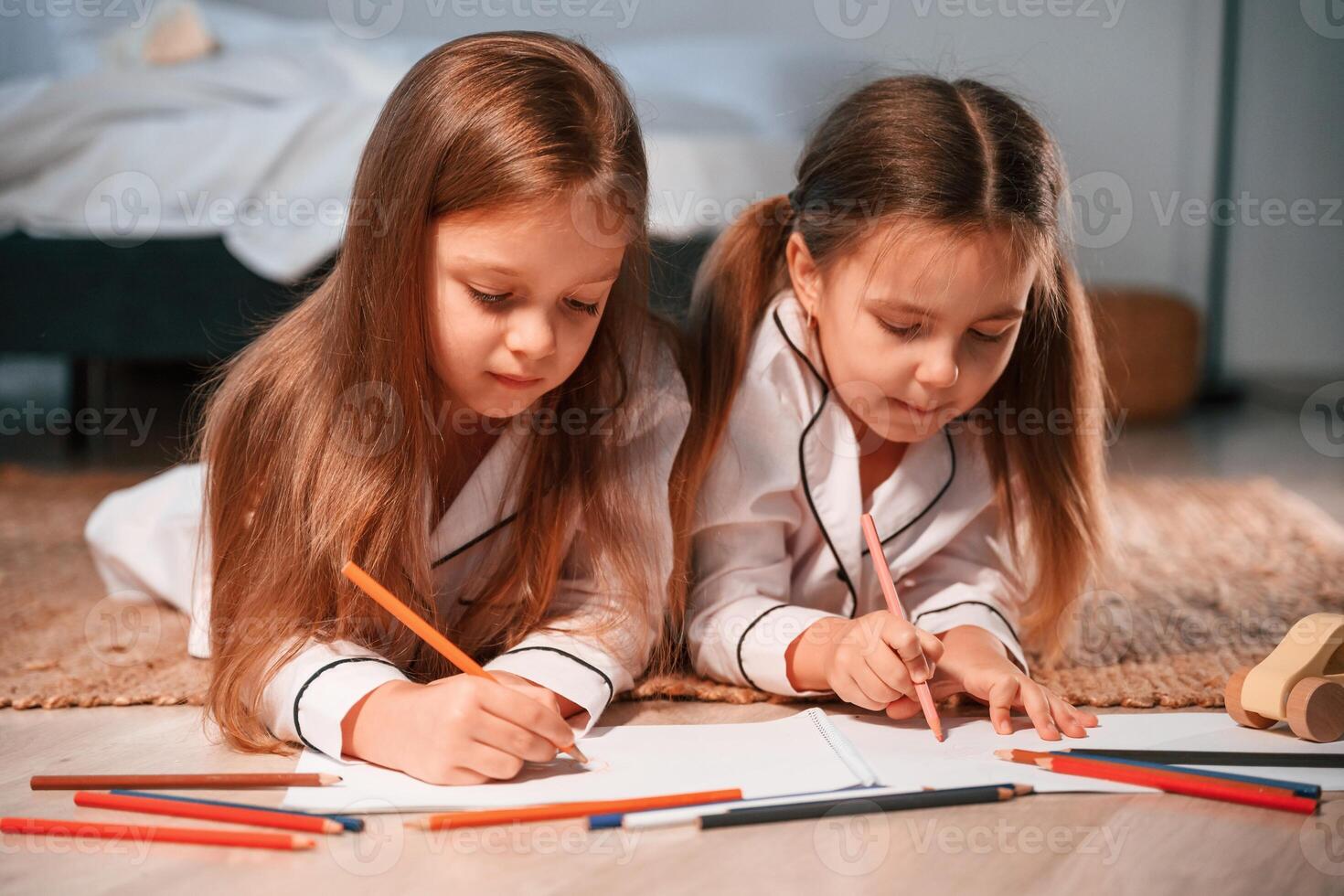Drawing, and lying down on the floor. .Two little girls are playing and having fun together in domestic room photo
