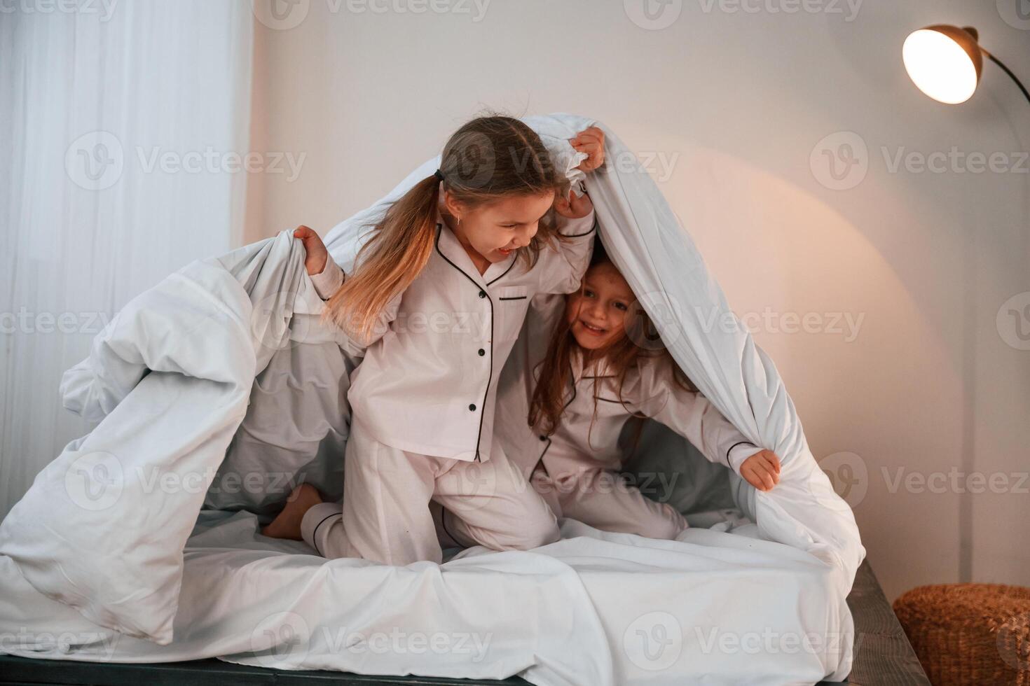 Holding the blanket. Two little girls are playing and having fun together in domestic room photo
