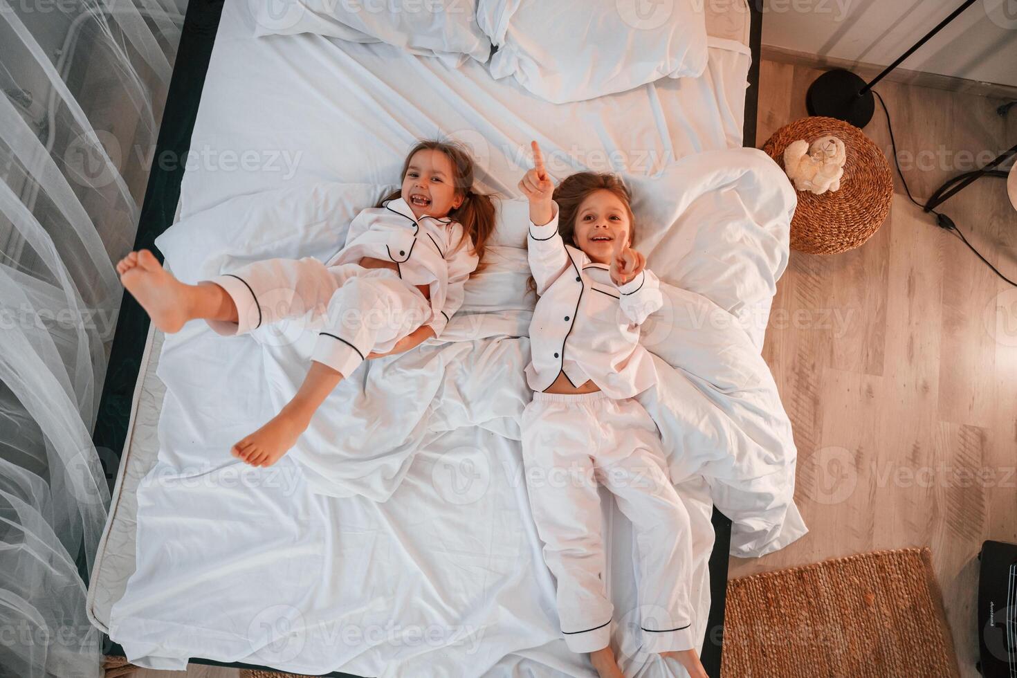 In the, bedroom. .Lying down. Two little girls are playing and having fun together in domestic room photo