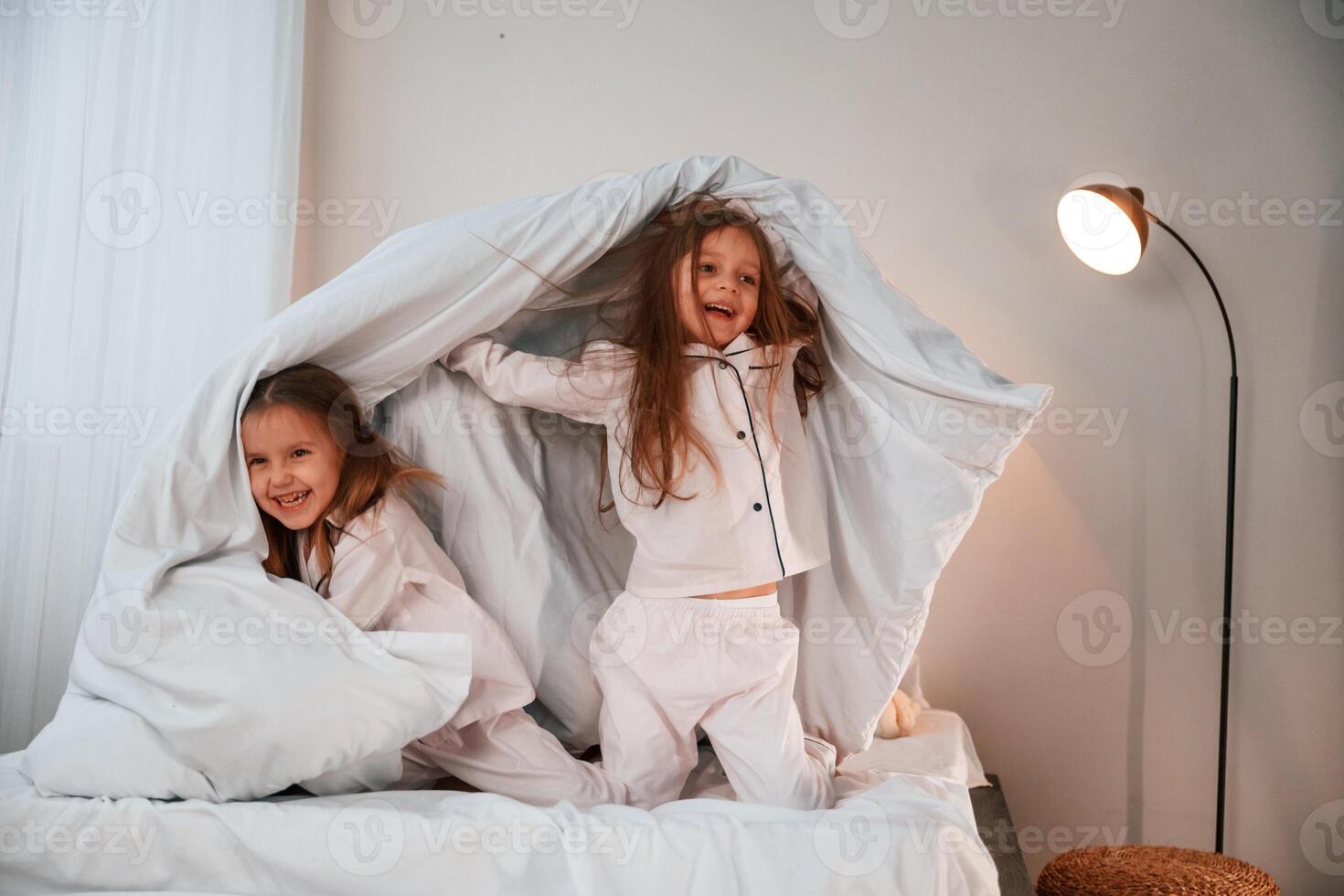 In the bedroom ,with blanket in hands. Two little girls are playing and having fun together in domestic room photo