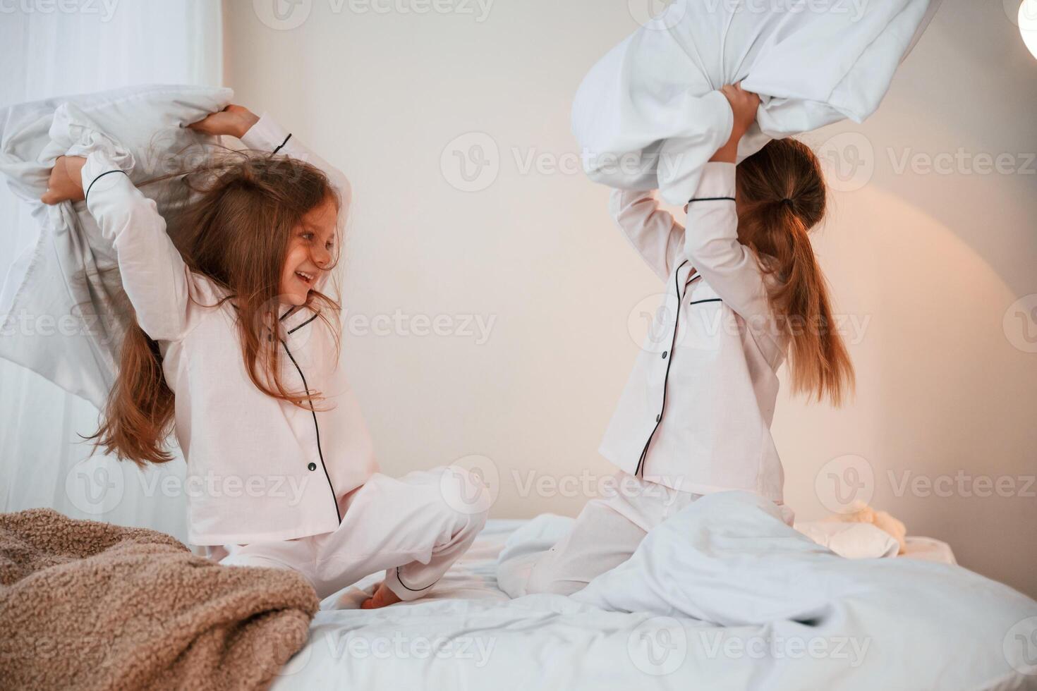 On the, bed. Pillow fight. Two little, girls are playing and having fun together in domestic room photo