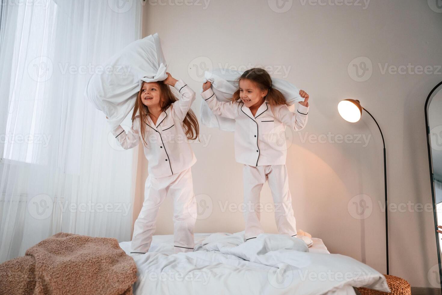 In, domestic room on the bed. Playing pillow fight. Two little girls are having fun together in domestic room photo