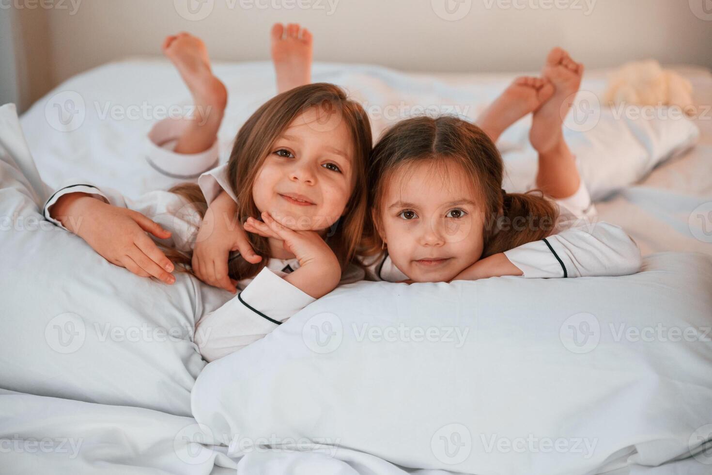 Smiling, laying down on the bed.. Two little girls are playing and having fun together in domestic room photo