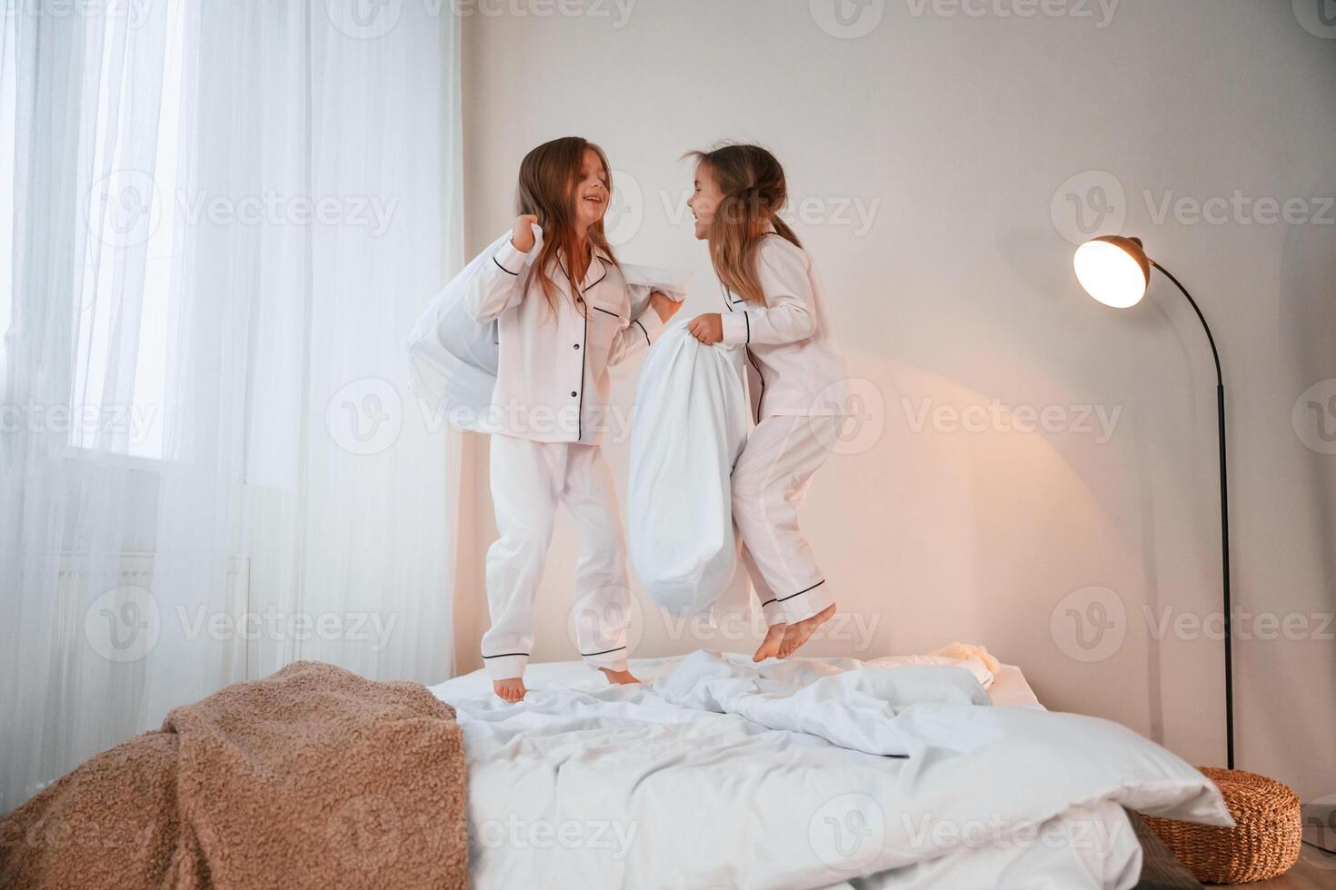 Holding pillows in hands. Two little girls are playing and having fun together in domestic room photo